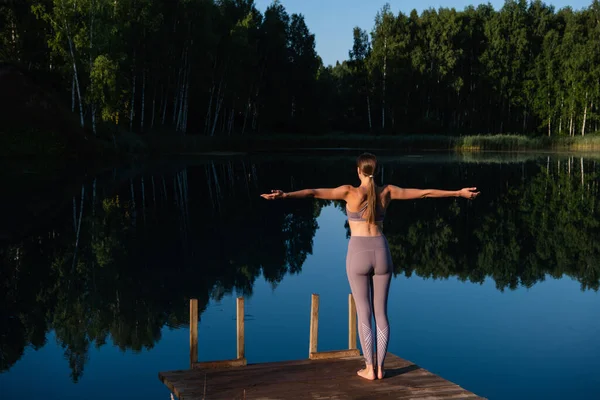 Young woman walks on wooden pier above forest lake scenery, preparing for morning yoga workout in nature. — Stock Photo, Image