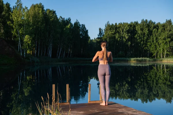 Молода жінка ходить по дерев'яному пірсу над пейзажами лісового озера, складає руки жестом-назвою. Жіночі руки, простягнуті в природі . — стокове фото