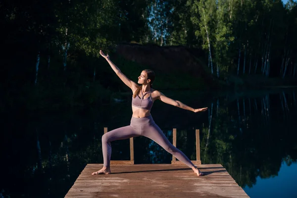 Beautiful young woman performing a spiritual yoga pose on a forest lake at sunny day, sunrise zen wellness — Stock Photo, Image