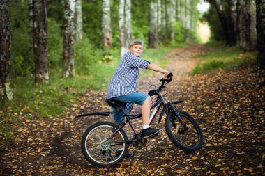 Orman yolunda bisiklet süren genç ve yakışıklı bir çocuk.