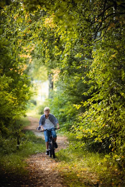 Preteen handsome boy with bicycle on the forest path — Stockfoto