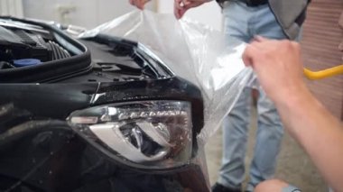 Servis ekibi garajda çalışırken koruyucu film uyguluyor. Bir araba yüzeyine poliüretan ppf uygulamak.
