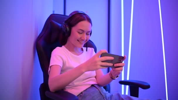 Young caucasian gamer girl sit on DxRacer chair and play online mobile game using Apple iPhone 11 Pro smart phone and livestreaming. Moscow - October 2020. — Stock Video