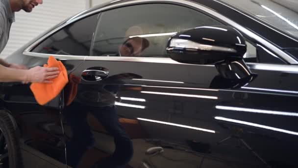 Trabajador está limpiando las puertas de lujo coche negro después de procesamiento protector y lavado en un garaje — Vídeos de Stock