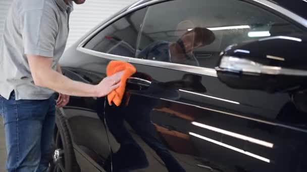 El hombre pule el coche, utiliza un paño de microfibra y pule para limpiar la carrocería de los coches. Limpiando intensamente la superficie del coche. — Vídeo de stock