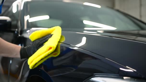 Ο άνθρωπος μετά το πλύσιμο σκουπίζει μαύρο αυτοκίνητο με ένα κουρέλι στο πλυντήριο αυτοκινήτων. Αρσενικό χέρι και το σώμα του αυτοκινήτου κοντά. — Αρχείο Βίντεο