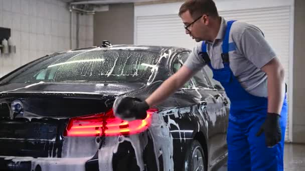 Detallado del coche - el hombre lava las luces traseras de un coche con una mano cubierta con un guante de lavado especial, primer plano. — Vídeos de Stock