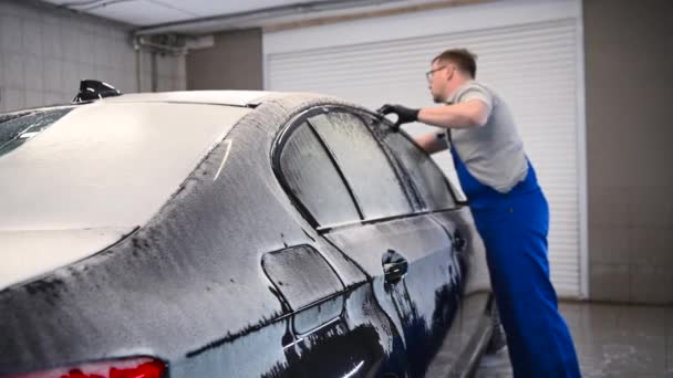 Un hombre haciendo lavado manual de coches en un coche negro con guante de limpieza especial. Lavado manual de autos portátil. Cuidado del coche detallado y suave. — Vídeos de Stock