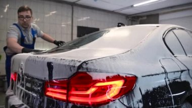 Kaportayı yıkadıktan sonra arabayı yıkayan adam özel bir temizlik eldiveniyle arabanın yüzeyini siliyor..