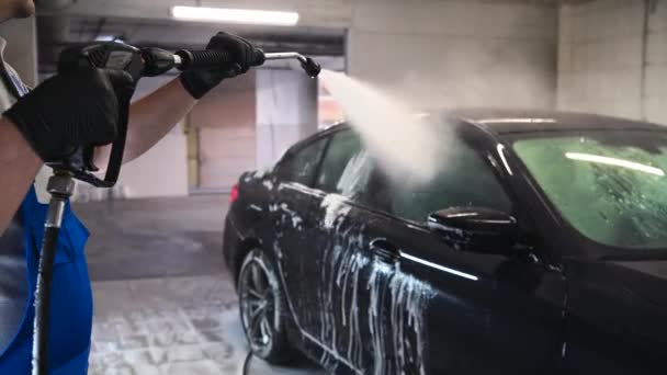 Миття та деталізація автомобілів. Професійний працівник миє чорний автомобіль за допомогою мийки під тиском на автомийці . — стокове відео