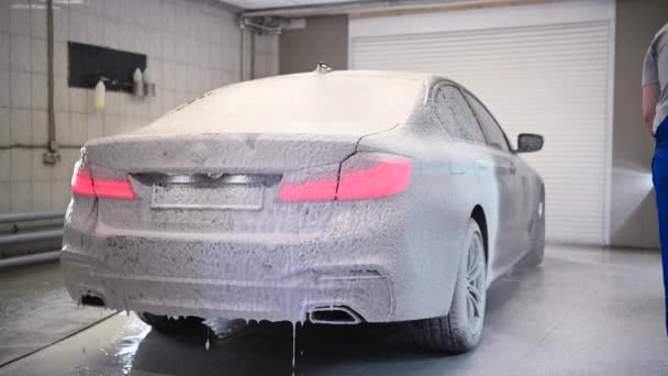 Especialista em automóveis masculinos cobrindo automóvel de luxo escuro com espuma no serviço de lavagem. Mecânico fazendo toda a preparação para a limpeza adequada do veículo moderno. — Vídeo de Stock