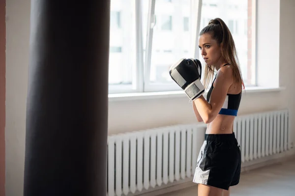 Dívka se připravuje na boxerskou soutěž a trénuje údery na boxovací pytel v prostorné tělocvičně — Stock fotografie