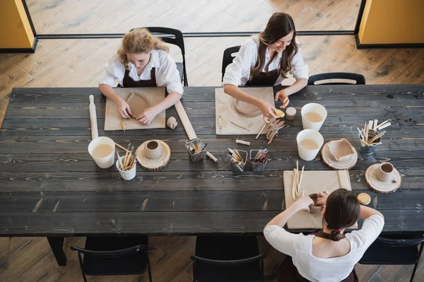 Young women learning to sculpt with a clay during a lesson at workshop in art studio.