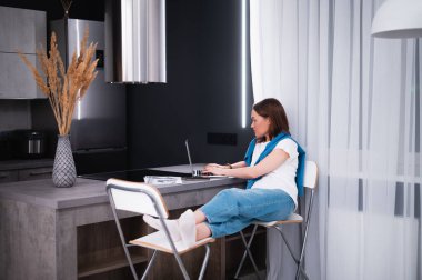 Yemek masasında uzaktan çalışan genç bir kadın. Arka planda ev mutfağı.