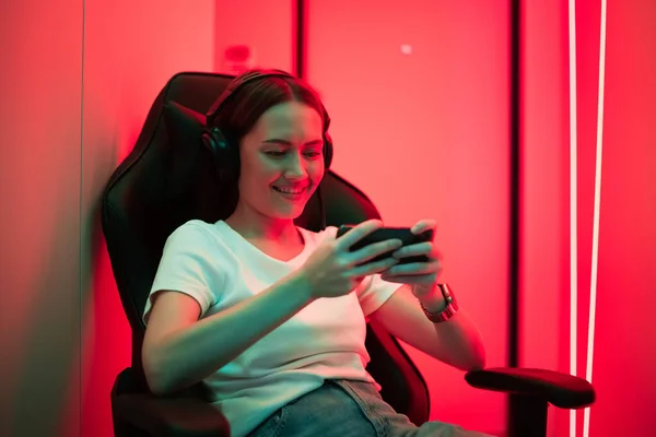 Cybersport-Gamer spielt Handyspiel auf dem Smartphone sitzend auf einem Gaming-Stuhl im neonfarbenen Raum. — Stockfoto