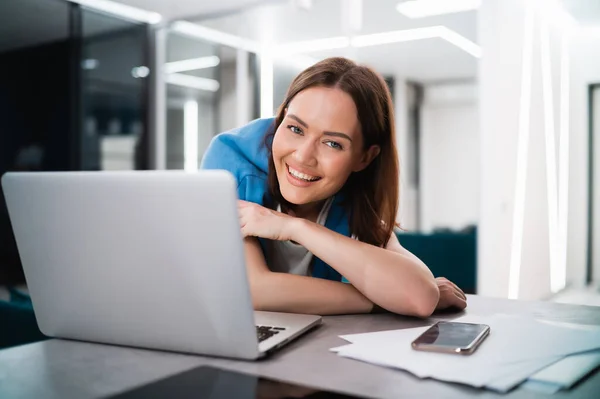 Uśmiechnięta młoda blogerka pracująca w domu. Happy girl pracuje zdalnie z domu siedzi przy biurku z laptopem i uśmiecha się do kamery. — Zdjęcie stockowe