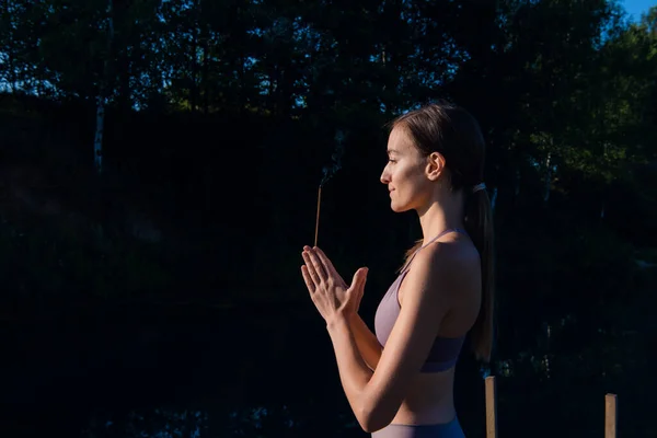 Young woman walks on wooden pier above forest lake scenery, folds her arms in a namaste gesture. Woman arms outstretched in nature. — Stock Photo, Image