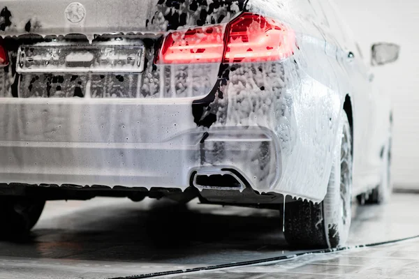 Coche con retroiluminación encendida de pie en el servicio de lavado de coches cubierto con una espuma. — Foto de Stock