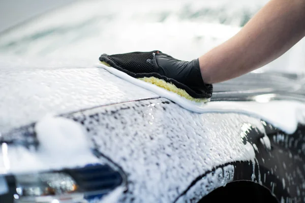 Hombre lavando un coche negro jabonoso en un servicio de limpieza y detalle. — Foto de Stock