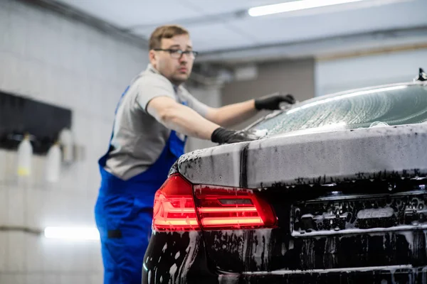 クリーニングと詳細サービスで黒い車の石鹸を洗う男. — ストック写真