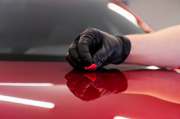 El maestro elimina pequeñas piezas de suciedad de la superficie del capó del coche con arcilla especial antes de pulir. Proceso profesional de lavado y detalle de automóviles. — Foto de Stock