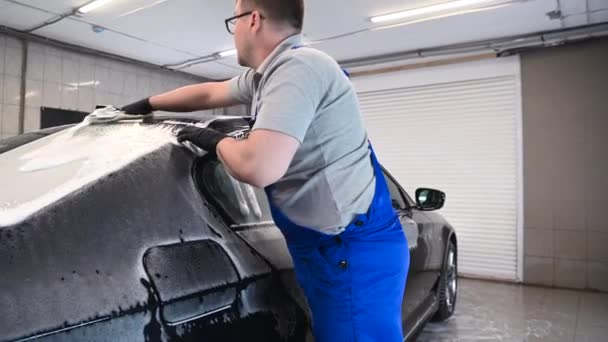 Мужчина, работающий в черной перчатке, моет машину с пеной. Концепция: Автосервис, Автомойка. — стоковое видео