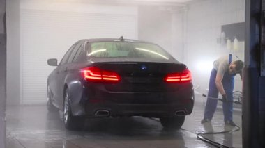 Garajda yüksek basınçlı su jetiyle siyah araba yıkayan bir adam. Bir otomobille ilgilenin..