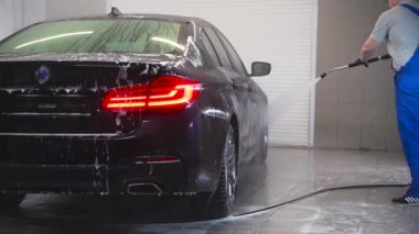 Garajda yüksek basınçlı su jetiyle siyah araba yıkayan bir adam. Bir otomobille ilgilenin..