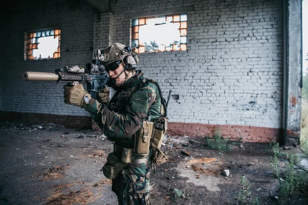 Voják v maskáčích s vojenskou zbraní mířící skrz zaměřovač pušky oknem staré budovy — Stock fotografie