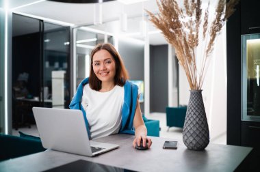 Mutfakta dizüstü bilgisayar kullanan genç bir kadın. Ev mutfağında defter üzerinde çalışan iş kadınının portresi. Ev işyerindeki bilgisayarda interneti arayan sıradan bir kız..