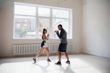 Tecrübeli bir antrenör boks salonunda genç bir kıza yumruk atma tekniğini uyguluyor.