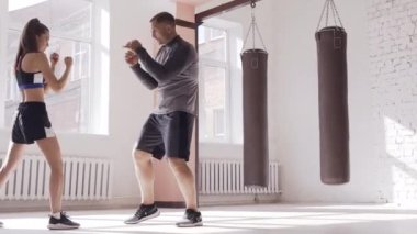 Tecrübeli bir antrenör boks salonunda genç bir kıza yumruk atma tekniğini uyguluyor.