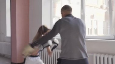 Genç bir kadının spor salonunda boks antrenmanı yaparken ve eğitmenini yumruklarken orta boy fotoğrafı.
