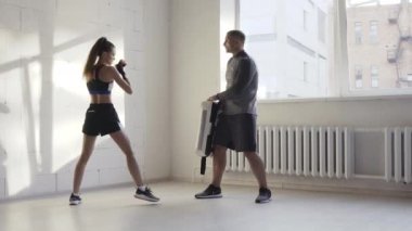 Antrenörle antrenman yapan kadın dövüş sanatları dövüşçüsü tekvando tekmesi egzersizi yapıyor. Kickboksçu kadının çıplak ayakla vurması, kum torbasını yumruklaması, kalkanı tekmelemesi.