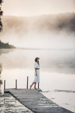 Serin bir sabahta gölde beyaz elbiseli genç bir kadın. Suyun üstünde bir sisle..