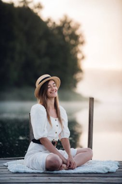 Beyaz elbiseli, açık havada oturan ve gülümseyen beyaz bir kadının portresi..