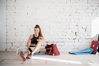 Profesyonel bir kadın boks ve kickboks koçu beyaz tuğla bir duvara karşı yerde yatıyor.