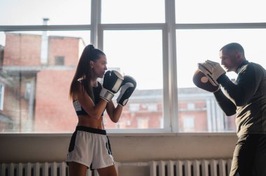 Kişisel antrenörle boks antrenmanı yapan bir kadın. Eğitmen kadın boksörlere birlikte dövüşmeyi öğretiyor.