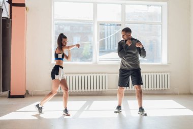 Genç bir kadının spor salonunda boks antrenmanı yaparken ve eğitmenini yumruklarken orta boy fotoğrafı..