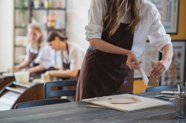 Çömlekçilik sınıfındaki genç bir kadın farklı aletlerle çalışıyor..
