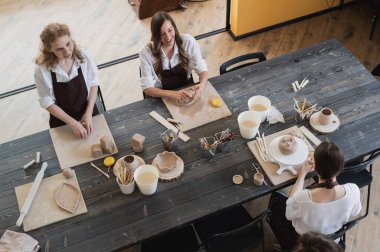 Kil atölyesindeki çalışma sırasında kadın çömlekçiler. Kadın ustalar büyük ahşap masada seramik ve kil ürünleri hazırlıyorlar.
