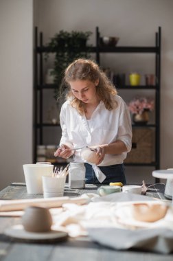 Dişi çömlekçi masada bir fırçayla boya karıştırıyor. Kadın seramik bir şey yapıyor. Çömlekçilik, el yapımı ve yaratıcı beceriler.