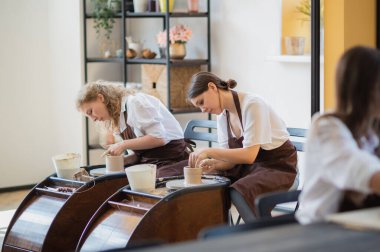 Sanat stüdyosundaki atölyede ders sırasında çömlek çarkında kille heykel yapmayı öğrenen genç kadınlar..