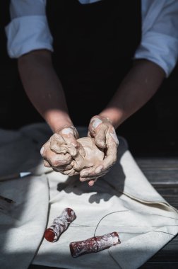 Islak eller çömlekçiden gri kille kaplanmış, işlenmemiş kil parçaları tutuyor.