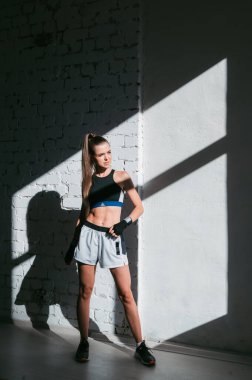 Çatı katında beyaz tuğladan bir duvarla genç ve fit bir kızın gölgesi ve ışık oyunuyla güzel zıt bir portre.