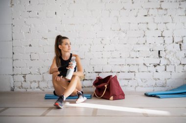 Kadın dövüşçü, egzersizden sonra susuz kalıp biberondan izotonik içecek içiyor. Genç bir kadın bir boks stüdyosunda yoğun bir eğitimden sonra dinleniyor..