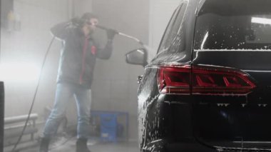 Garajda yüksek basınçlı su jetiyle siyah araba yıkayan bir adam. Bir otomobille ilgilenin..