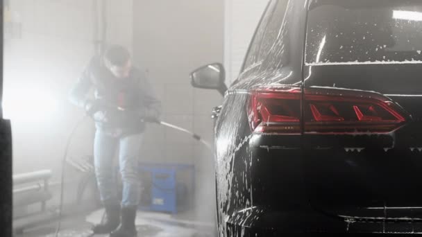 Make worker washing black car arches under high pressure water after foam application. Concept: Auto Car Service, Car Wash, Cleaning Machines. — Stock Video