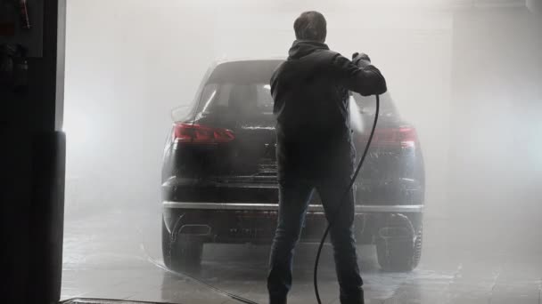 Férfi permetező víz a nagynyomású mosó, hogy mosson egy autót az autószerelő műhelyben. — Stock videók