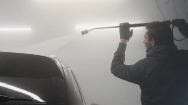 Araba yıkama ve temizlik. Profesyonel bir işçi araba yıkama makinesinde siyah bir arabayı yıkıyor..